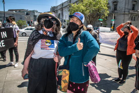white older woman in Mask Together America tee stands with Asian 30-something who gives a thumbs up